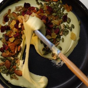 Bạn mở lửa nhỏ riu riu và cho hạt óc chó, hạnh nhân, hạt bí, nho khô, dứa khô, mứt nam việt quất và đảo đều hỗn hợp sau đó tắt bếp.